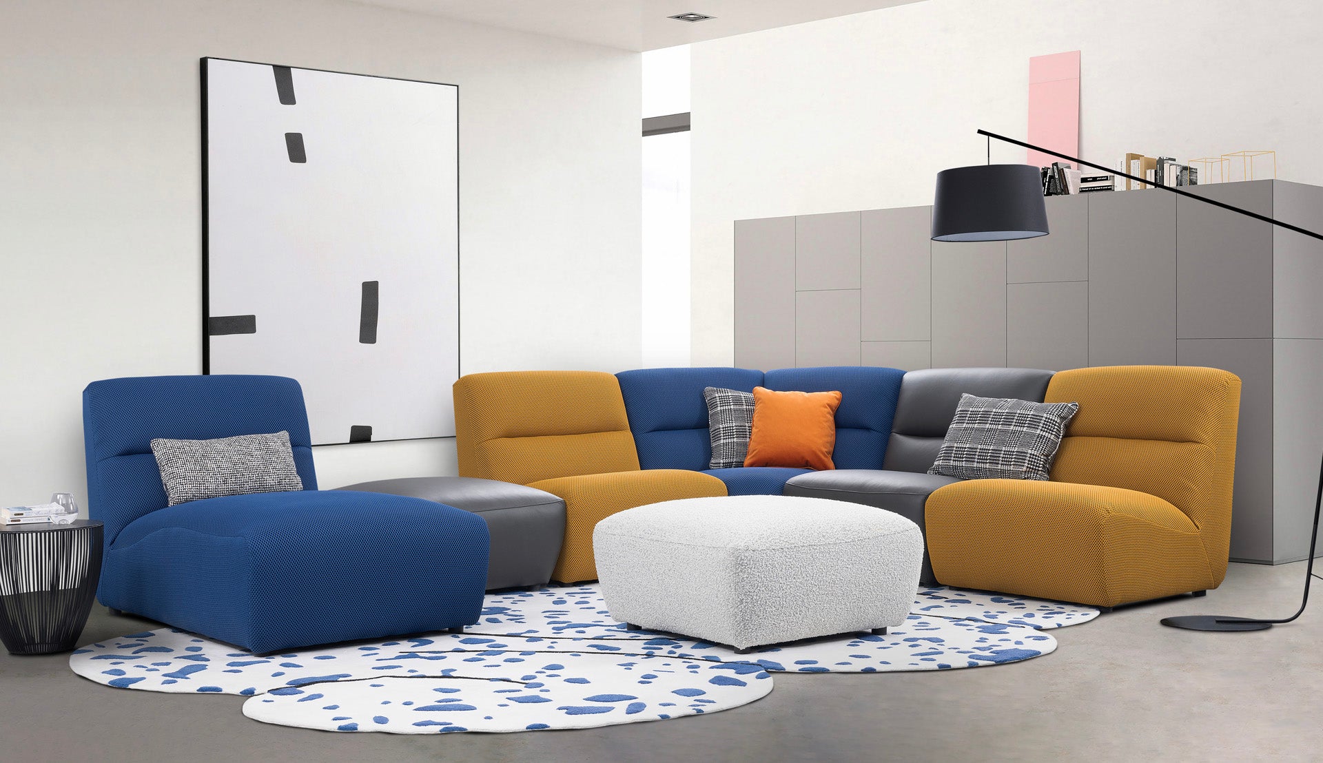 Modern living room with a blue and yellow sectional sofa, ottoman, and decorative pillows.