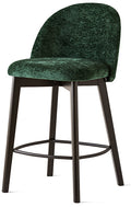 A modern bar stool featuring a dark green velvet upholstered seat and curved backrest, supported by a dark brown wooden four-leg base with a circular metal footrest.