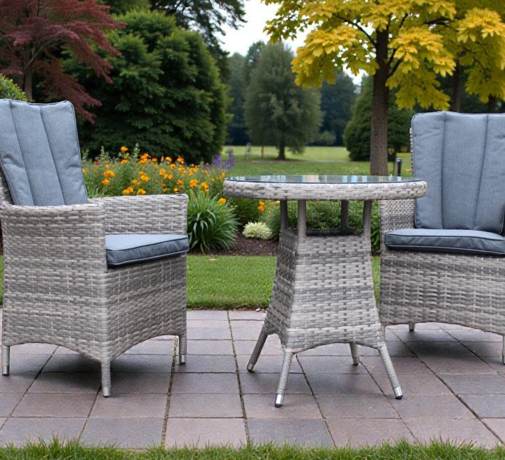 A man and a woman sit at a round outdoor bistro table with cups, surrounded by woven gray patio chairs with blue cushions on a white background.