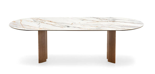 An oval dining table with a white marble-look top featuring subtle gray and warm gold veining, supported by two sturdy, tapered brown wooden legs, shown against a plain white background.