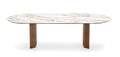 An oval dining table with a white marble-look top featuring subtle gray and warm gold veining, supported by two sturdy, tapered brown wooden legs, shown against a plain white background.