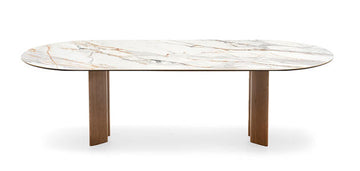 An oval dining table with a white marble-look top featuring subtle gray and warm gold veining, supported by two sturdy, tapered brown wooden legs, shown against a plain white background.
