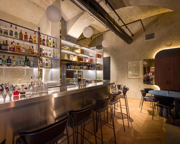 Modern bar interior with shelves of bottles, stools, and a counter.