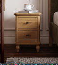 Wooden nightstand with two drawers, a mug, and books in a bedroom setting.